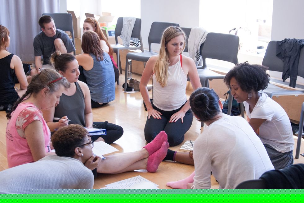 Women of various ages and ethnicities sit on the floor in a circle with notes.